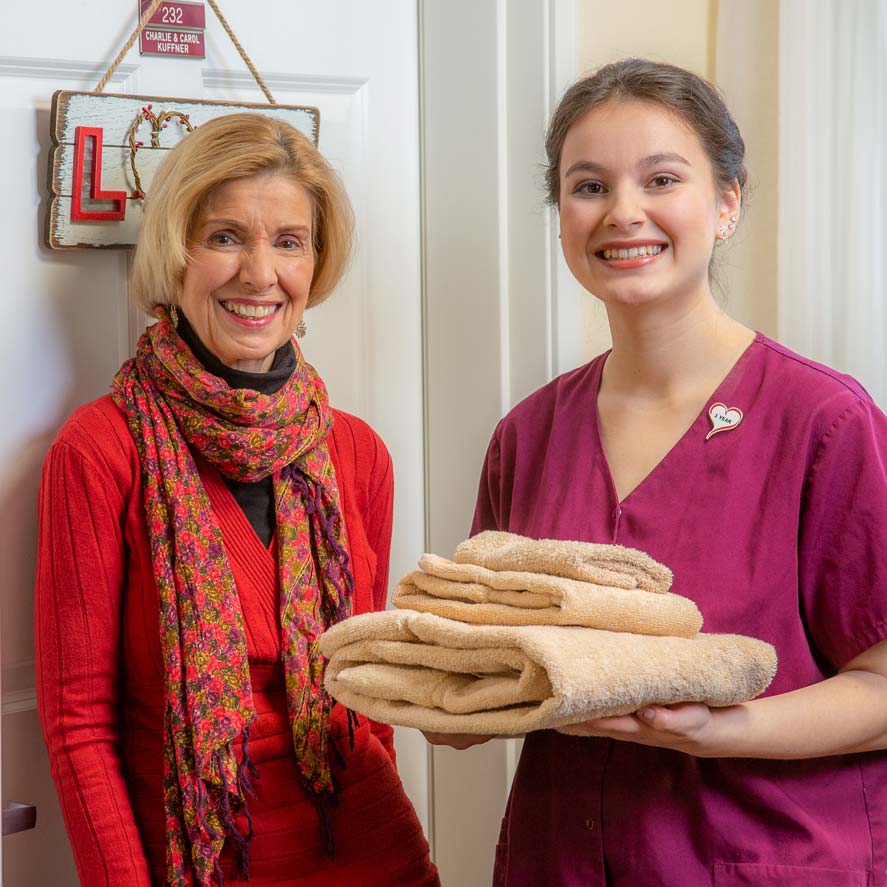A team member delivering fresh linens to a resident at The Lodge at Wake Forest